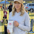 Woman holding a white soccer Mom tumbler with a logo at a soccer event