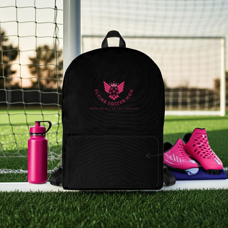 Black soccer mom backpack with pink logo on grass in front of a soccer goal