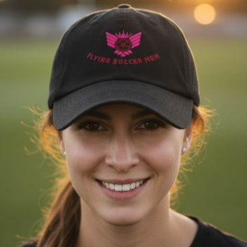Soccer mom wearing a black cap with pink text and logo, standing outdoors.